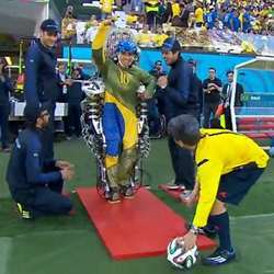 A paralyzed young man using a thought-controlled exoskeleton to help him kick a soccer ball.