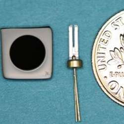 Vahala's new laser frequency reference (left) is a 6mm disk; the quartz "tuning fork" (center) is the frequency reference commonly used in watches. The dime at right is for scale.
