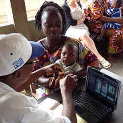 A health official in Benin, Africa, scans a babys fingerprints for entry into a vaccination database.