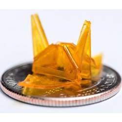 A tiny origami structure created through a self-folding process is shown on a quarter for size comparison.