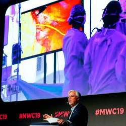 Dr. Antonio Maria de Lacy speaking at Mobile World Congress 2019, with the surgery proceeding on the screen behind him.