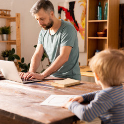 father works at laptop computer as son watches