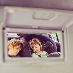 vehicle vanity mirror shows two kids sleeping in backseat