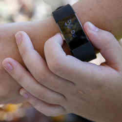 A student adjusts her fitness tracker at the park where she does her jogging workouts for her "online PE" class.
