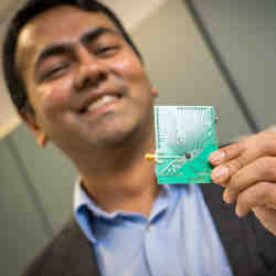 UC San Diego electrical and computer engineering professor Dinesh Bharadia holds a printed circuit board; the Wi-Fi radio is mounted underneath the black blob.