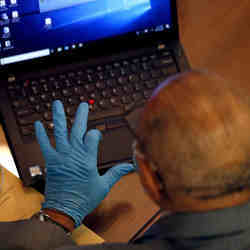 A man wearing gloves works on a laptop.