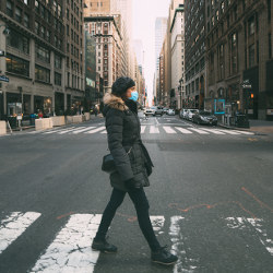 person wearing winter coat and face mask crossing city street