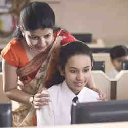 A teacher oversees her student's work on a computer. 