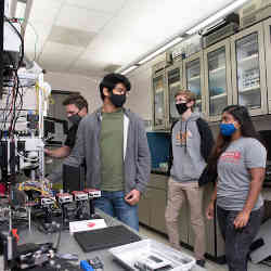 An interdisciplinary team of students conducts quantum research in an integrated photonics laboratory. 