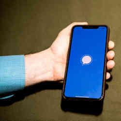 A hand holding a smartphone bearing the Signal app icon.