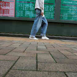A passerby holding a smartphone walks past screens showing market indices outside a brokerage in Tokyo, Japan.