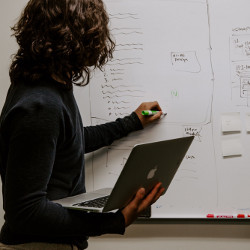 person writing on whiteboard while holding a laptop computer