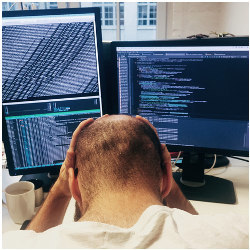 man with head in hands in front of two computer screens