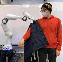 A robot assists a test subject in putting on a vest.