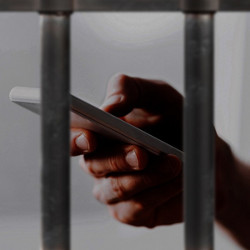 hand holding cellphone behind prison bars