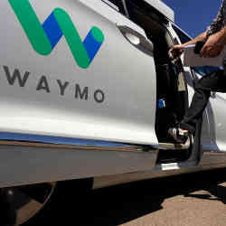 A customer steps into a self-driving Waymo vehicle. 