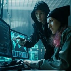 Photo of male and female hackers working on computers to perform malicious acts