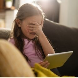 Photo of little girl using a tablet computer covers her eyes from what's onscreen.