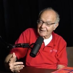 A screen shot of Donald Knuth speaking into a microphone as he's being interviewed