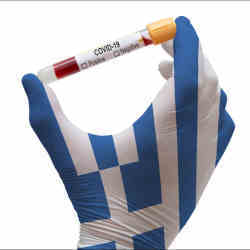 A hand clad in the colors of Greece holds a test tube containing a COVID test. 