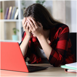 student with head in hands at laptop computer