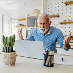 Bearded man yells at laptop in frustration and anger.