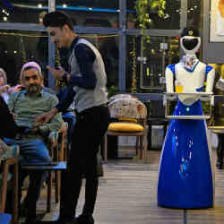 A robot waiter carries food orders to patrons' tables. 