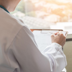 person in whitecoat consults a medical reference clipboard