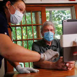 A nurse helps set up a telehealth session for William Merry, a patient recovering from pneumonia, at home in Ipswich, MA.