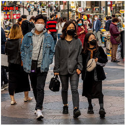 masked couple and a young girl walk on a crowded street