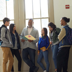 diverse group of students stand with an instructor in a hallway