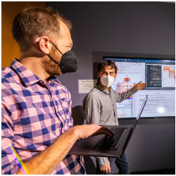 Sandia researchers Andrew Baczewski and Erik Nielsen at a wall-mounted display screen