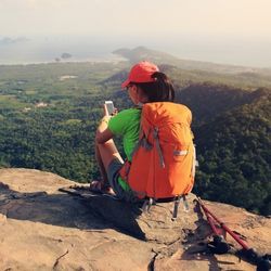 Person using smartphone on mountaintop overlooking landscape.