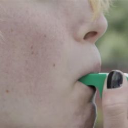 Close-up photo of woman blowing a whistle.