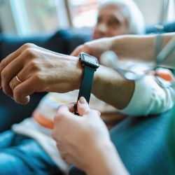 Healthcare professional assists patient with putting on a wearable health monitor bracelet.