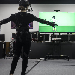 performer in motion-capture suit in front of a screen showing her virtual character