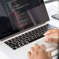 programmer's hands on a keyboard of a laptop computer displaying code