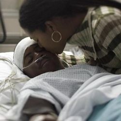 Woman kissing child who is in intensive care in hospital bed.