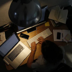 remote worker typing on a keyboard under a desk lamp