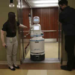 Hospital staffers hold elevator doors for a Moxi robot.