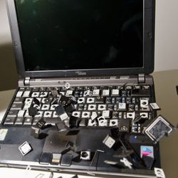 An old laptop has all of its keys smashed and scattered.