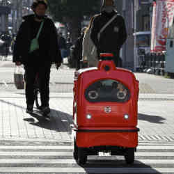 A four-wheeled robot dodges pedestrians on a street outside Tokyo.