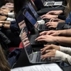 Hands of several people type on their laptop computers in a classroom setting.