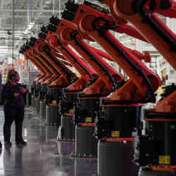 A woman next to robotic arms for a battery tray assembly line at the opening of a Mercedes-Benz electric vehicle battery factory in Woodstock, AL.