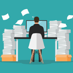 worker at computer surrounded by stacks of papers