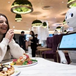 A restaurant patron sitting at a table interacts with a robot waiter.