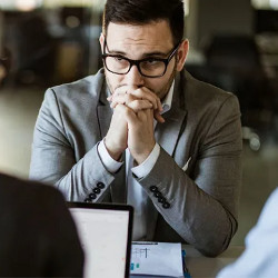 uncertain interviewee holds his folded hands in front of his chin