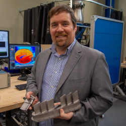 Penn State's Stephen Lynch holds metal 3D-printed turbine vanes.