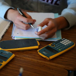 three calculators on the desk of a student writing in a math notebook