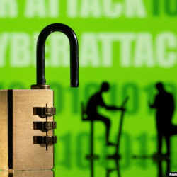 Three-dimensionally printed models of people working on computers and a padlock,  in front of a display of binary code and the words CYBER ATTACK.  